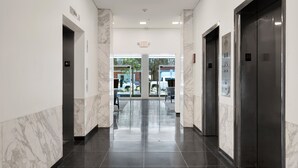A modern hotel corridor with marble walls, black tiled floors, and two elevators. - Luxury Downtown Retreat | Heated Pool Access (Savannah)