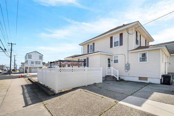 A two-story residential house with a white exterior, a front porch, and a small fenced area. - 4BR Shore House-Close To The Action (North Wildwood)
