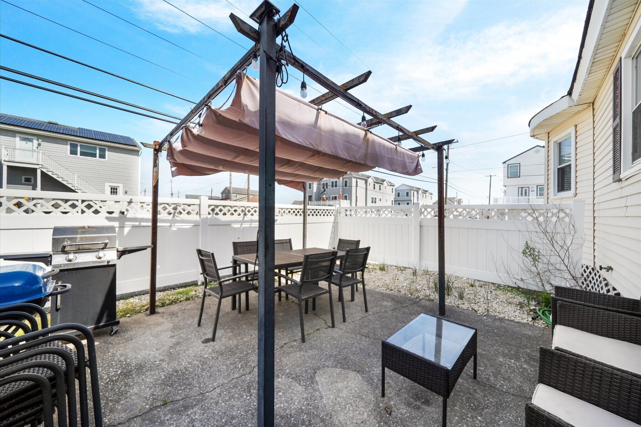 Un patio con mesa y sillas, una parrilla y un pérgola con toldo.