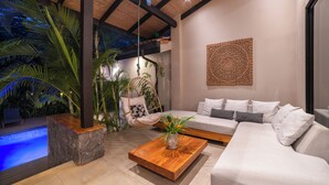 A modern living room with a stone coffee table, a hanging chair, a sofa, and a decorative wall piece. - Villa in Hacienda Pinilla Near Beach – Private Pool, Golf Cart & Beach Club Access Included (Tamarindo)