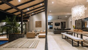 A spacious living area with a high ceiling, a dining table, sofas, and a large chandelier. - Villa in Hacienda Pinilla Near Beach – Private Pool, Golf Cart & Beach Club Access Included (Tamarindo)
