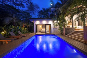 A modern pool area with a glass-enclosed spa room, wooden deck, and lounge chairs. - Villa in Hacienda Pinilla Near Beach – Private Pool, Golf Cart & Beach Club Access Included (Tamarindo)