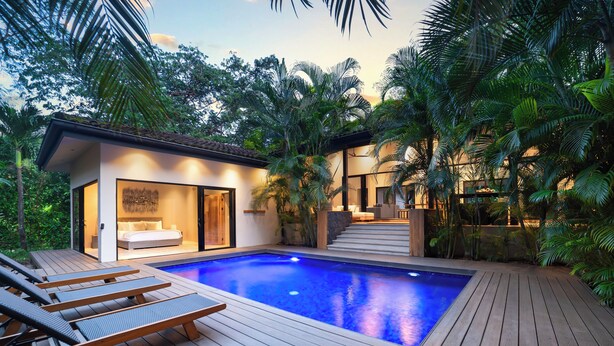 A modern pool area with wooden deck and lounge chairs, surrounded by lush greenery. - Villa in Hacienda Pinilla Near Beach – Private Pool, Golf Cart & Beach Club Access Included (Tamarindo)
