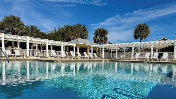 A pool area with white lounge chairs and a covered seating area.