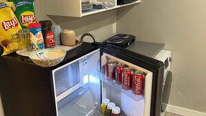 A compact kitchen with a refrigerator, microwave, and a small countertop. - RaphaSuites (Regina)