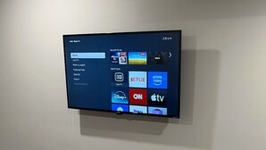 A flat-screen TV mounted on a wall displaying a streaming service interface with various app icons. - RaphaSuites (Regina)