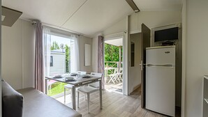 A compact kitchenette with a built-in refrigerator, a dining area with a table and chairs, and a view of the outdoor garden. - L'avocette by Interhome (Carnac)