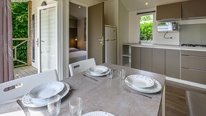 A modern kitchen with a dining area, including a table set for four, a refrigerator, and a window with a view of greenery. - L'avocette by Interhome (Carnac)