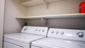 A laundry area with two front-loading washing machines and a shelf above them. - Eagle's guest suits: two bedrooms living room private kitchen and full washroom (Victoria)