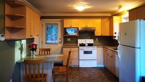 A kitchen with wooden cabinets, a white stove, a refrigerator, and a dining area with a chair and a vase of flowers. - Eagle's guest suits: two bedrooms living room private kitchen and full washroom (Victoria)