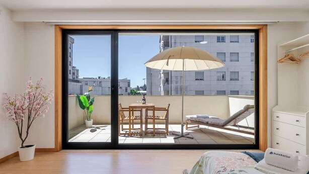 A bedroom with a large sliding glass door leading to a balcony with a table and chairs, a lounge chair, and a hanging chair. - Stylish Studio w/ Balcony & Garage by HostWise (Porto)
