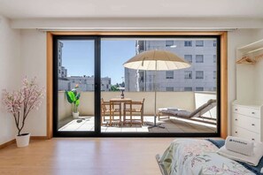 Une chambre dotée d’une grande porte-fenêtre coulissante donnant sur un balcon aménagé avec une table et des chaises, un fauteuil et un fauteuil suspendu.
