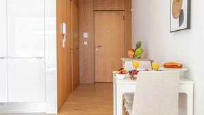 A modern kitchen with white cabinets, a wooden door, and a breakfast setup with fruits and juice. - Stylish Studio w/ Balcony & Garage by HostWise (Porto)