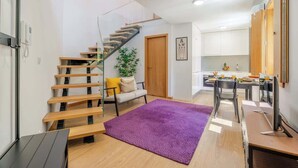 A modern kitchen with white cabinets, a wooden staircase, and a purple rug. - Stylish Duplex w/ Garage by HostWise (Porto)
