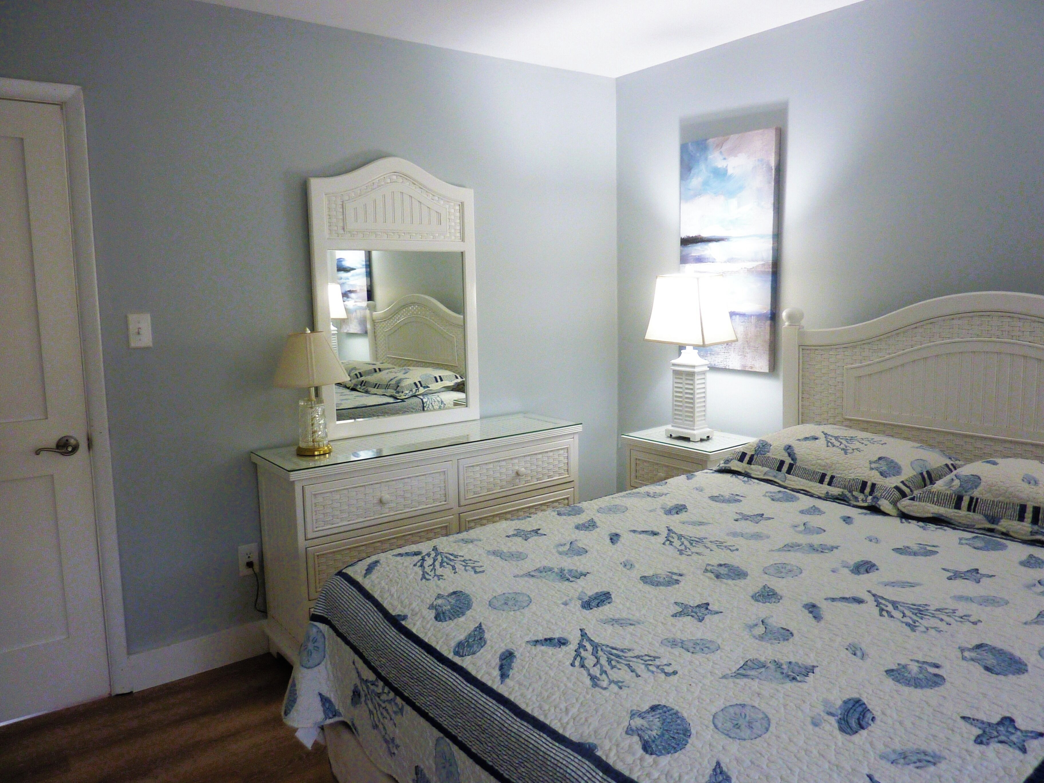 A bedroom with a bed, a dresser, a mirror, and a nightstand with a lamp.