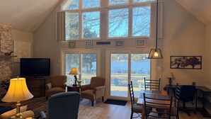 Een ruime woonkamer met een hoge plafond, grote ramen, een televisie, comfortabele zitplaatsen en een eethoek.