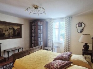 Classic bedroom with a bed, nightstand, and wardrobe, featuring a framed picture and window with curtains.