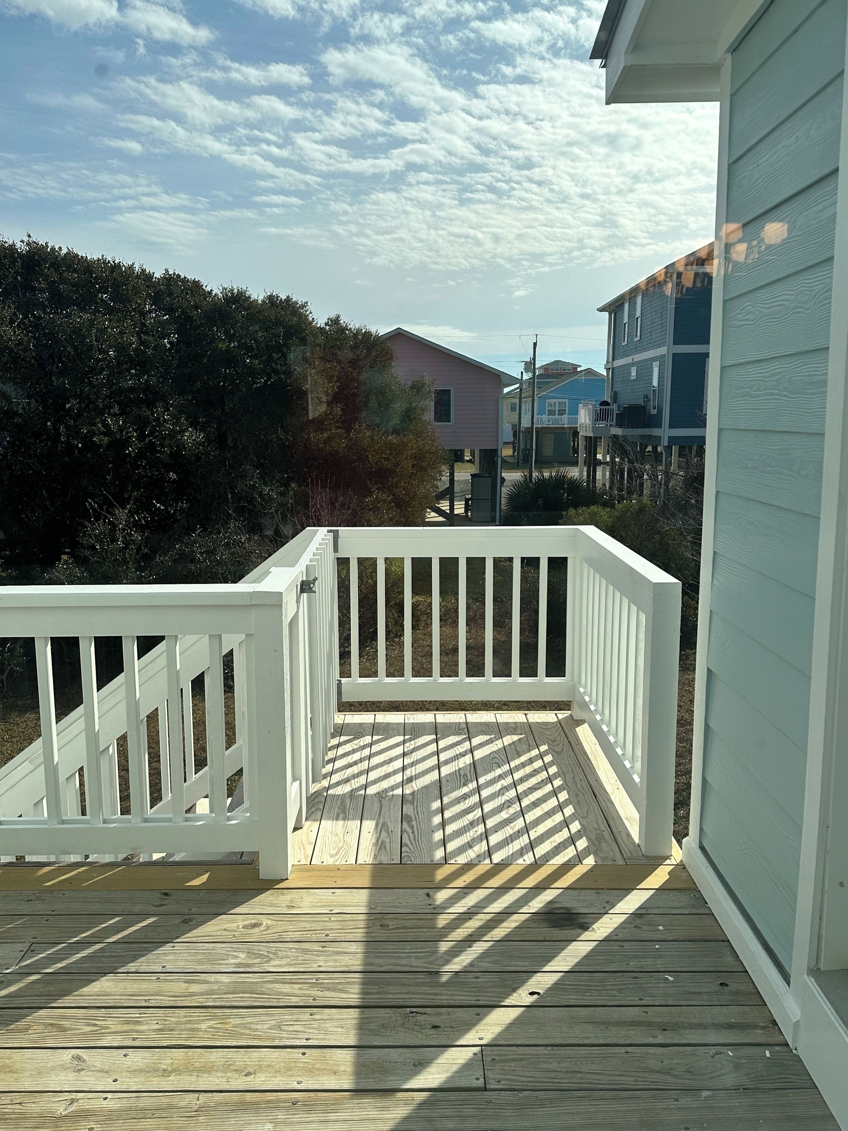 A wooden deck with a white railing, leading to a building with a light blue exterior.