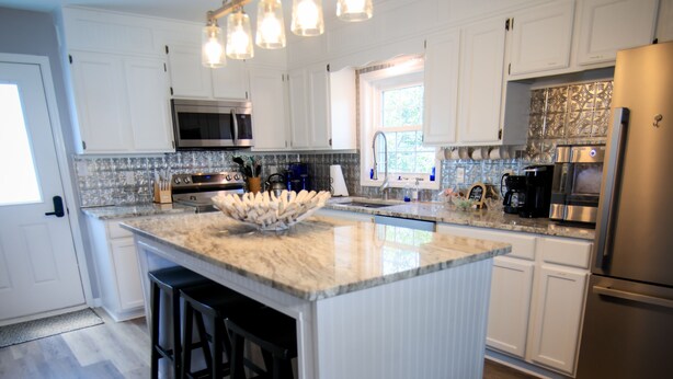 A modern kitchen with white cabinetry, a large island with stools, stainless steel appliances, and a hanging light fixture. - 3-bedroom house in fantastic family-friendly Surf City, 2 min walk to the beach. (Surf City)