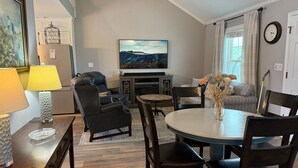 A modern living room with a flat-screen TV, a dining table, and comfortable seating. - 3-bedroom house in fantastic family-friendly Surf City, 2 min walk to the beach. (Surf City)