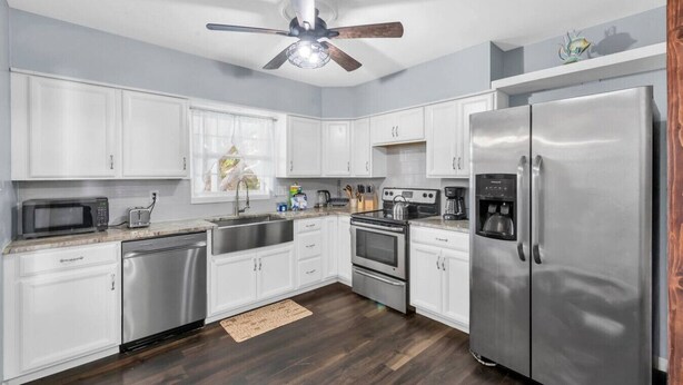 Una cocina moderna con gabinetes blancos, electrodomésticos de acero inoxidable, un ventilador de techo y piso de madera.