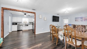 Una cocina moderna con armarios blancos, un comedor con mesa y sillas de madera, y una sala de estar con un sofá marrón.