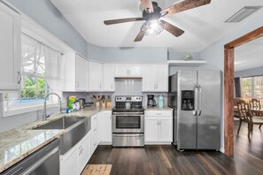 A modern kitchen with white cabinets, stainless steel appliances, and a ceiling fan.