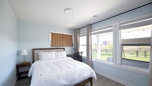 Ein Schlafzimmer mit Bett, Nachttisch, Lampe und Blick ins Freie.