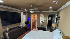 Une chambre avec un grand lit, une télévision, un ventilateur de plafond et un dressing.