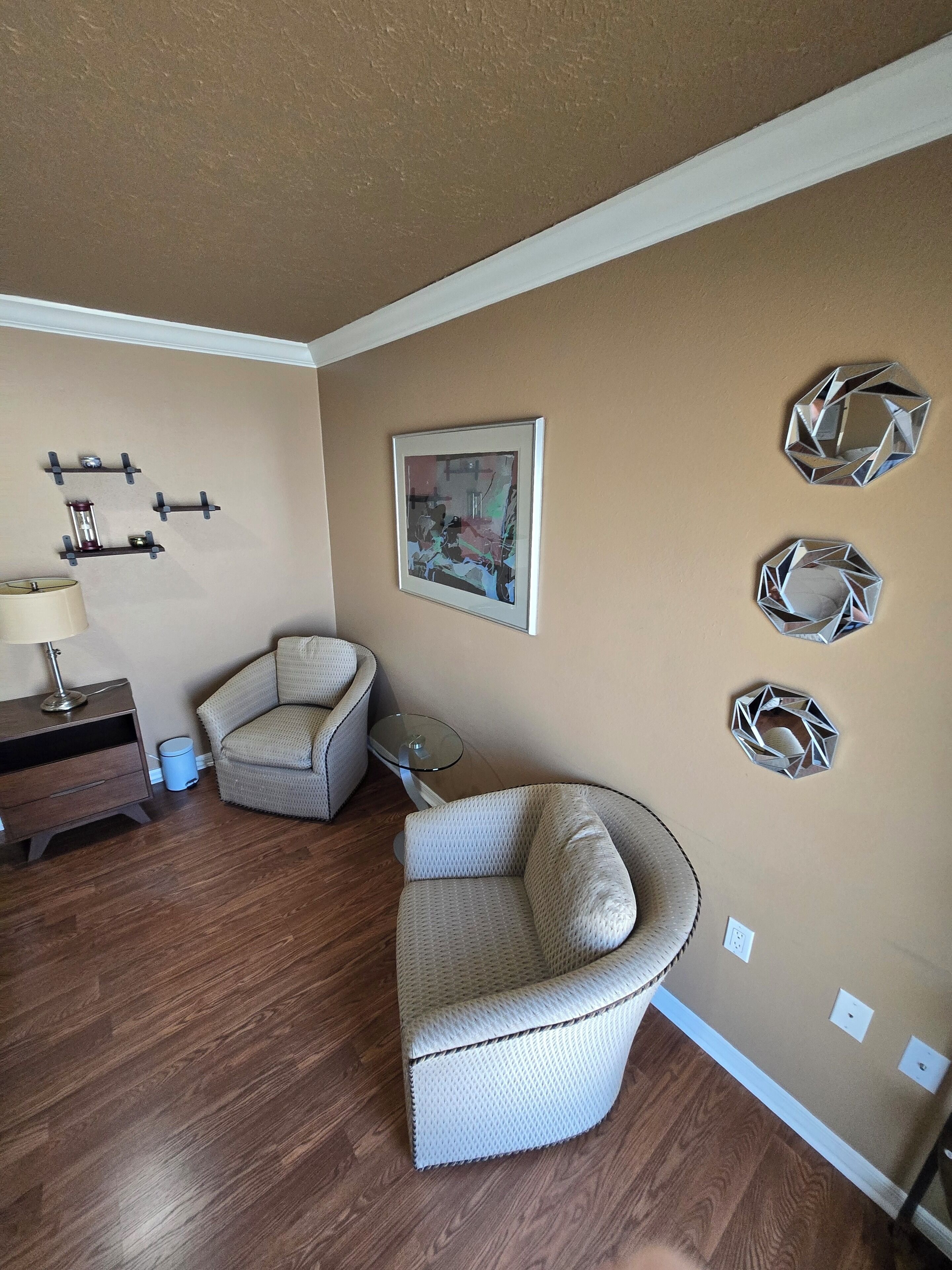 A living room with a brown wall, a framed painting, and three geometric wall decorations.