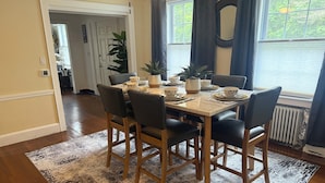 Un coin repas avec une table dressée pour quatre personnes, entourée de chaises, d’un tapis à motifs et de plantes en pot.