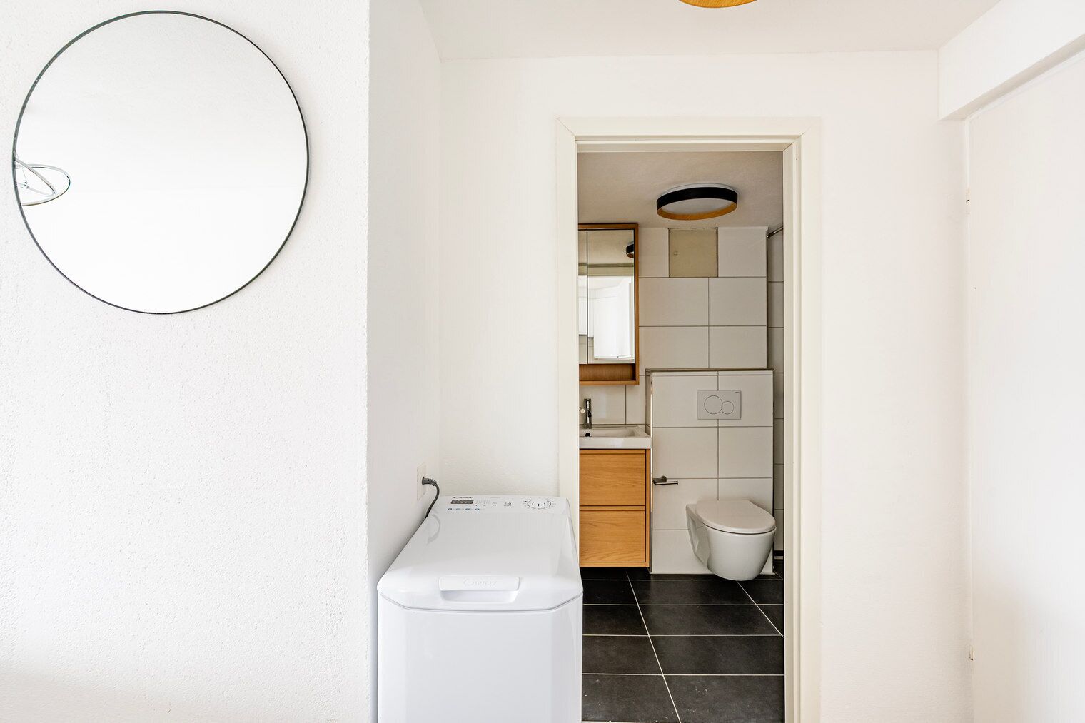 Een kleine badkamer met toilet, wastafel en een rond spiegel aan de muur.