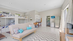 Una habitación moderna y bien iluminada con sofá, literas, televisor y zona de cocina.