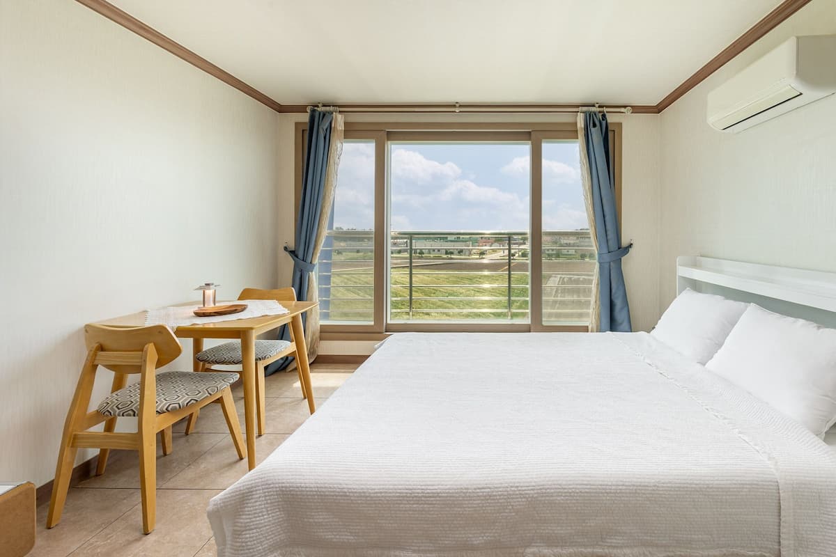 A hotel room with a bed, a small table with a chair, and a window with curtains.