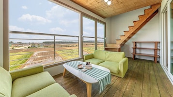 A room with a large window, a wooden staircase, and a green sofa.