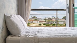 Un dormitorio con cama, almohada y vista a una zona industrial por la ventana.