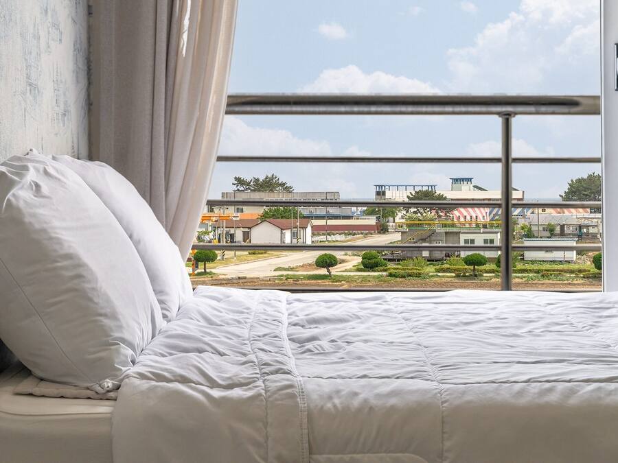 Ein Schlafzimmer mit einem Bett, einem Kopfkissen und Blick auf ein Industriegebiet durch ein Fenster.