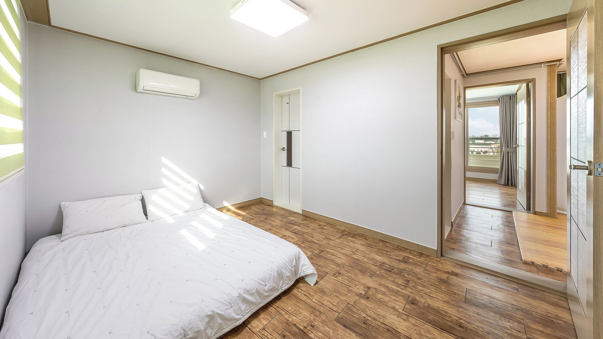 Una camera da letto con un letto, un condizionatore bianco, una porta e vista su uno spazio esterno attraverso una porta aperta.