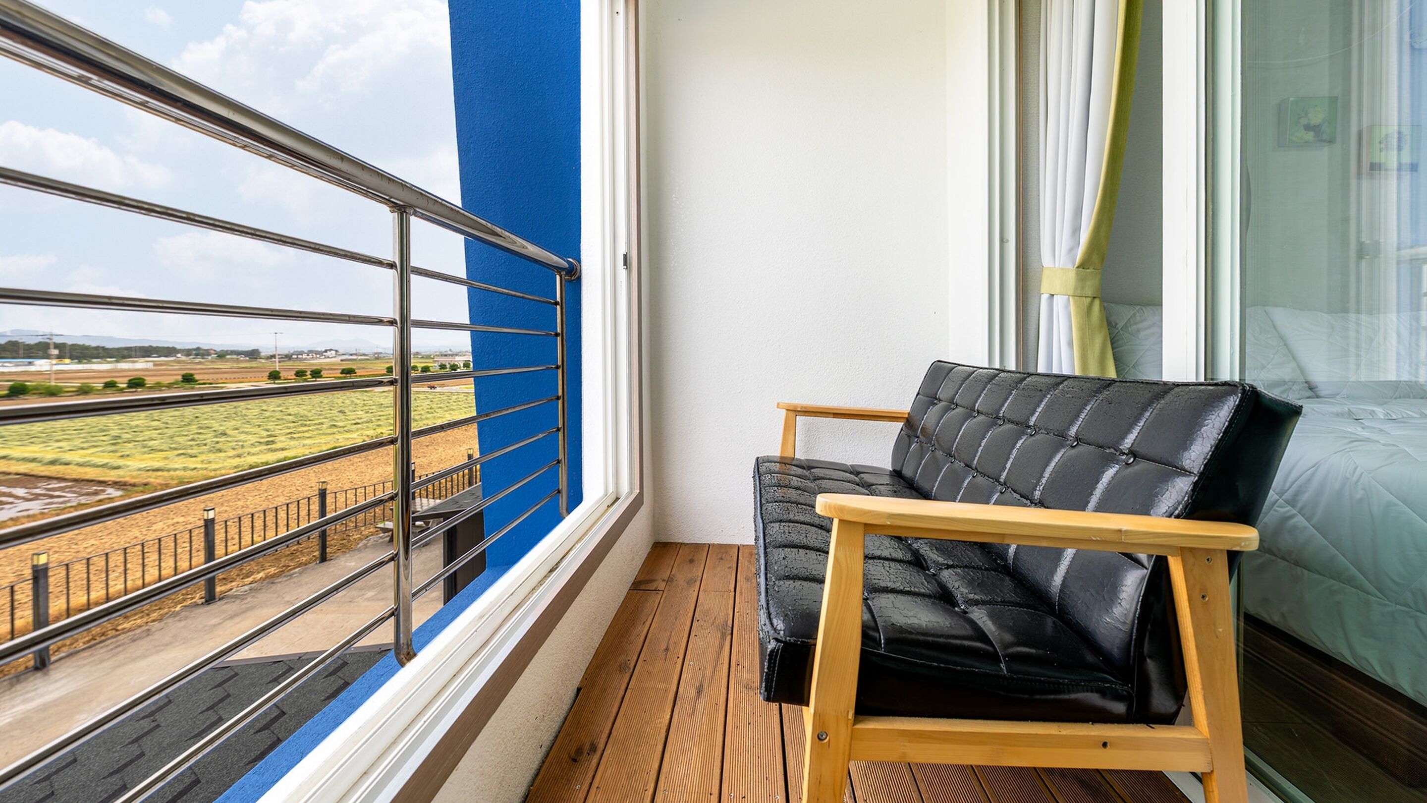 Ein Balkon mit Blick auf ein Feld, ein schwarzer Ledersessel und ein Bett mit einem grünen Vorhang.