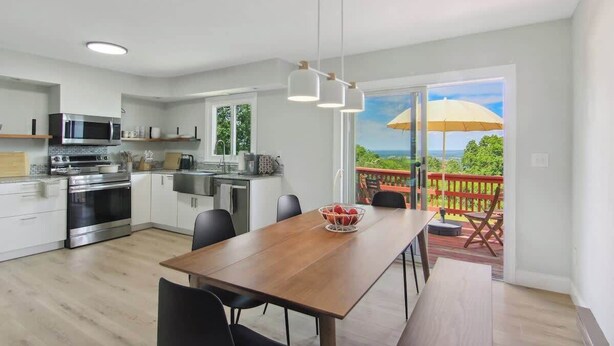 Una cocina moderna con electrodomésticos de acero inoxidable, un comedor con mesa de madera y un balcón con barandilla roja y sombrilla amarilla.