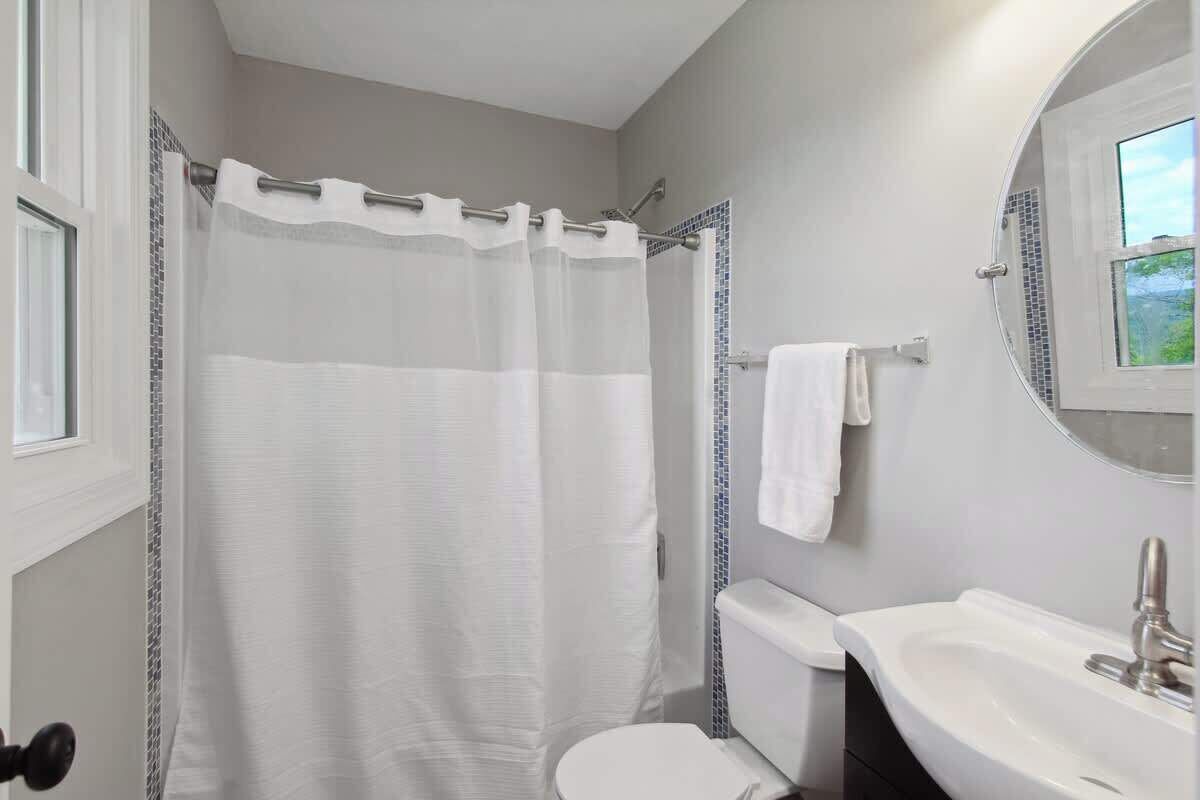 A bathroom with a shower curtain, toilet, sink, and a window.