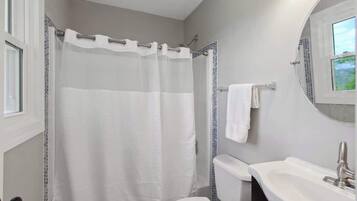 A bathroom with a shower curtain, toilet, sink, and a window.