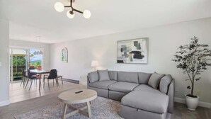 Una sala de estar moderna con un sofá seccional gris, una mesa de centro redonda y una zona de comedor con sillas.