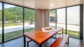 A modern dining area with a wooden table, benches, and a view of a park and building through large windows.