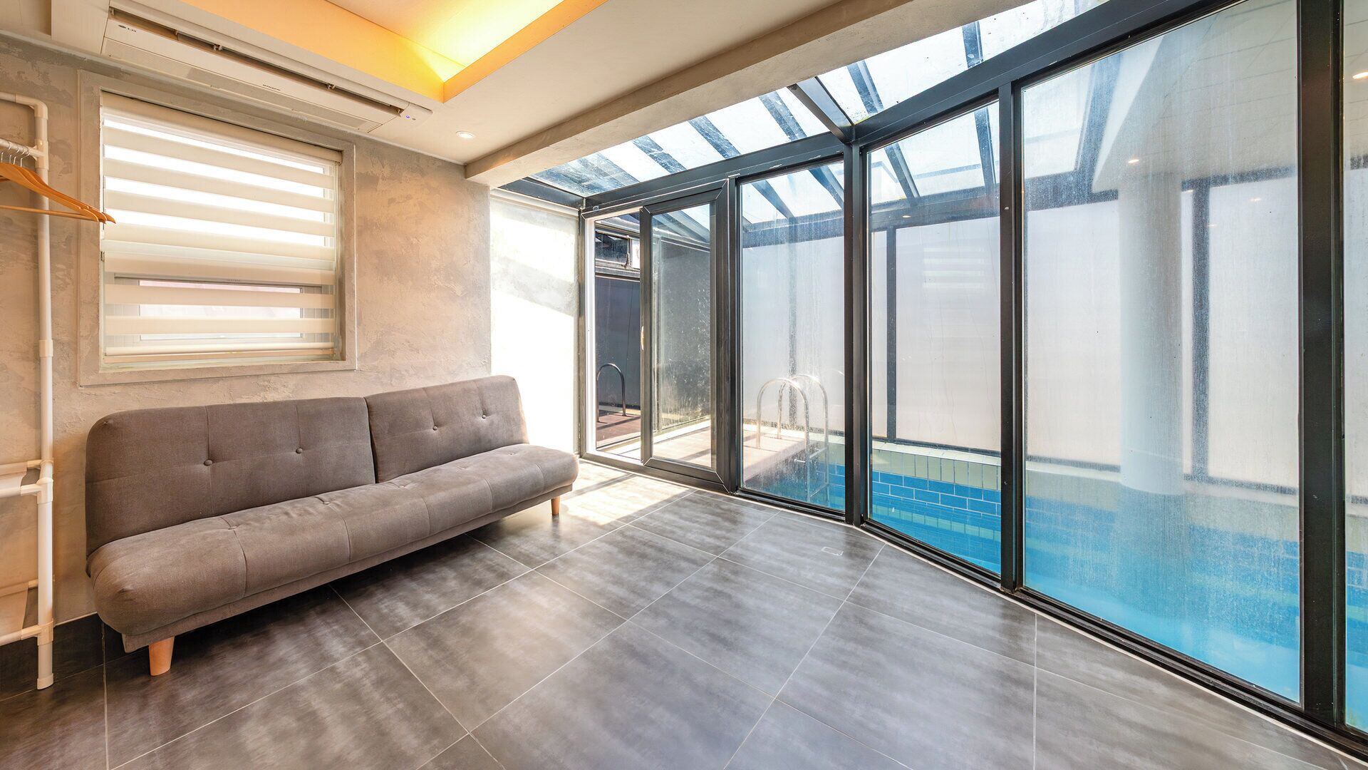 Un interior moderno con un sofá gris, un amplio ventanal y vistas a una piscina exterior.