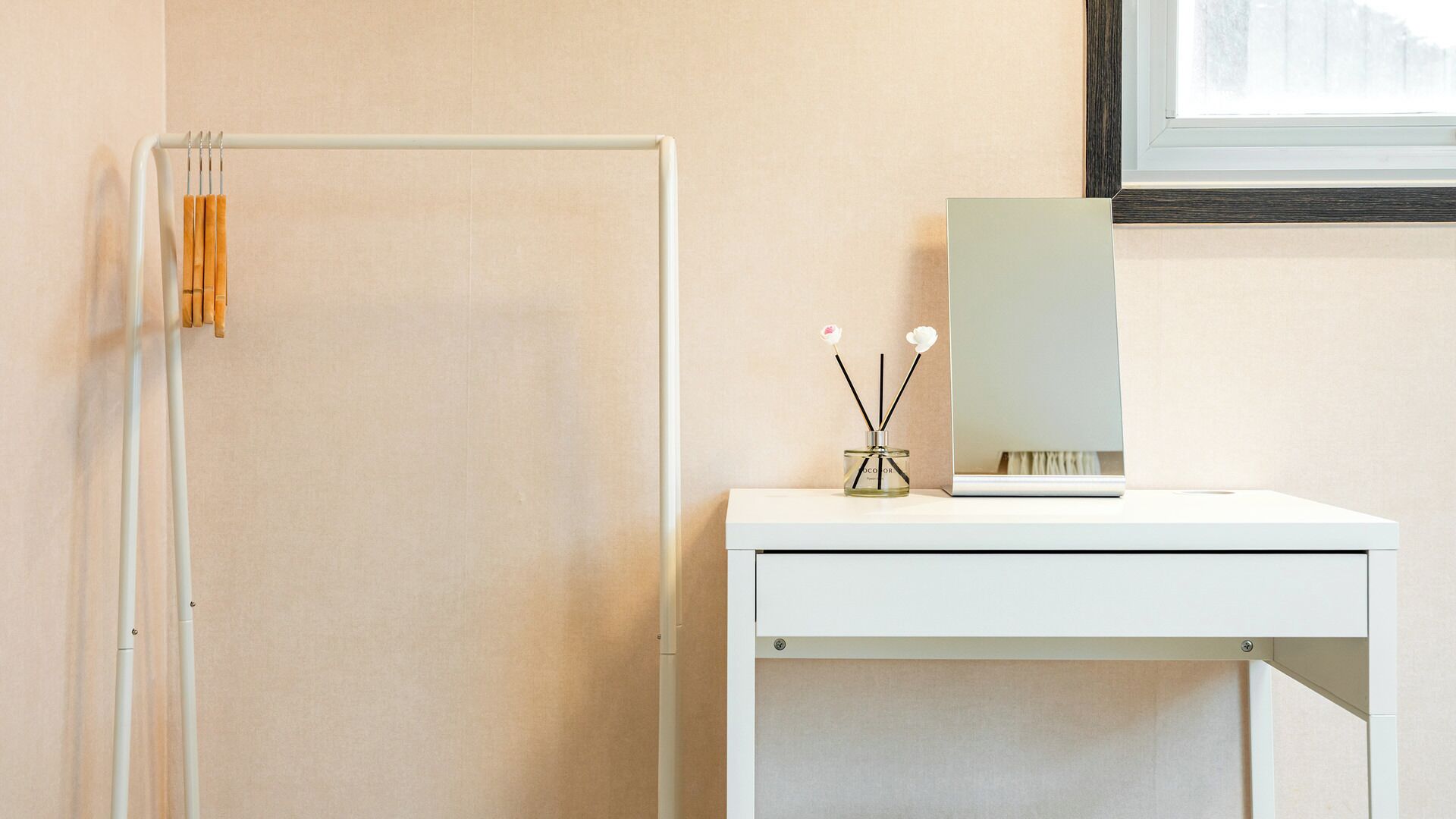 A minimalist bathroom with a white vanity, a mirror, and a small table with a bottle and two sticks.