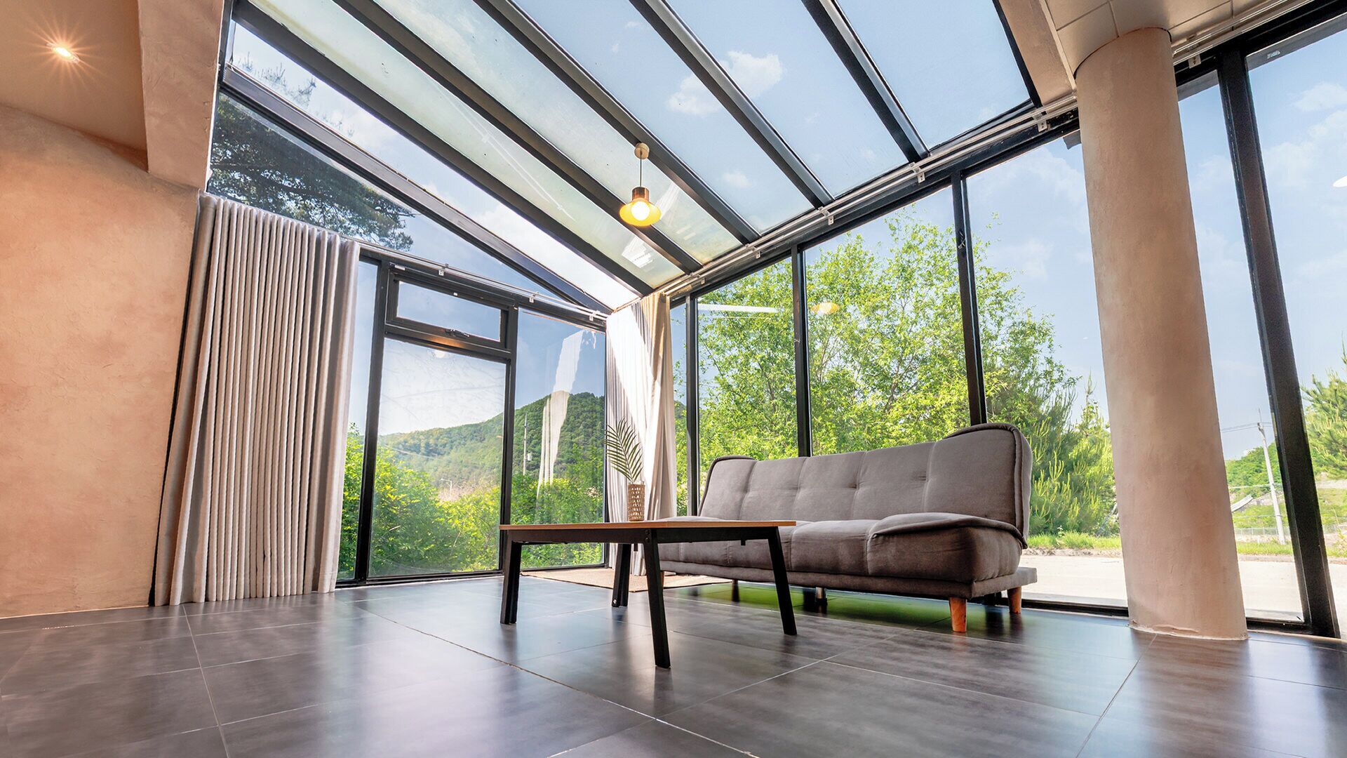 Un interior moderno con sofá, mesa y grandes ventanales que ofrecen vistas al verdor.