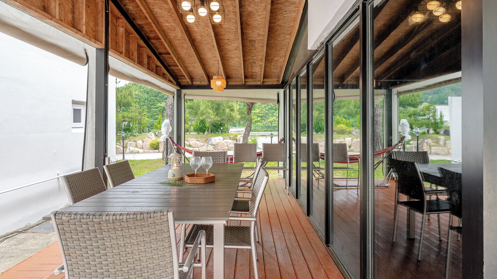 Un área de comedor al aire libre con una mesa larga y sillas, una lámpara colgante y vistas del paisaje circundante.