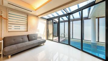 A modern living room with a grey sofa, a glass door leading to a pool, and a skylight above.