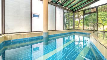 A swimming pool with clear blue tiles, large windows, and a view of greenery outside.